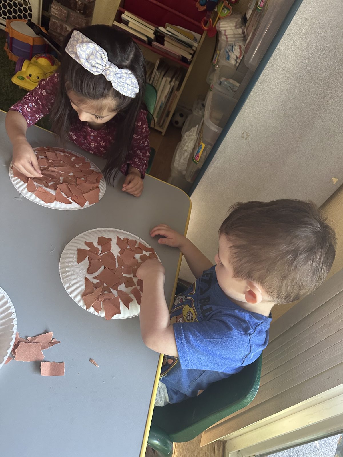 Two children gluing torn paper onto paper plates for a craft project