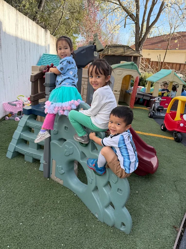 Three toddlers climbing and smiling on backyard play equipment at Crayoland