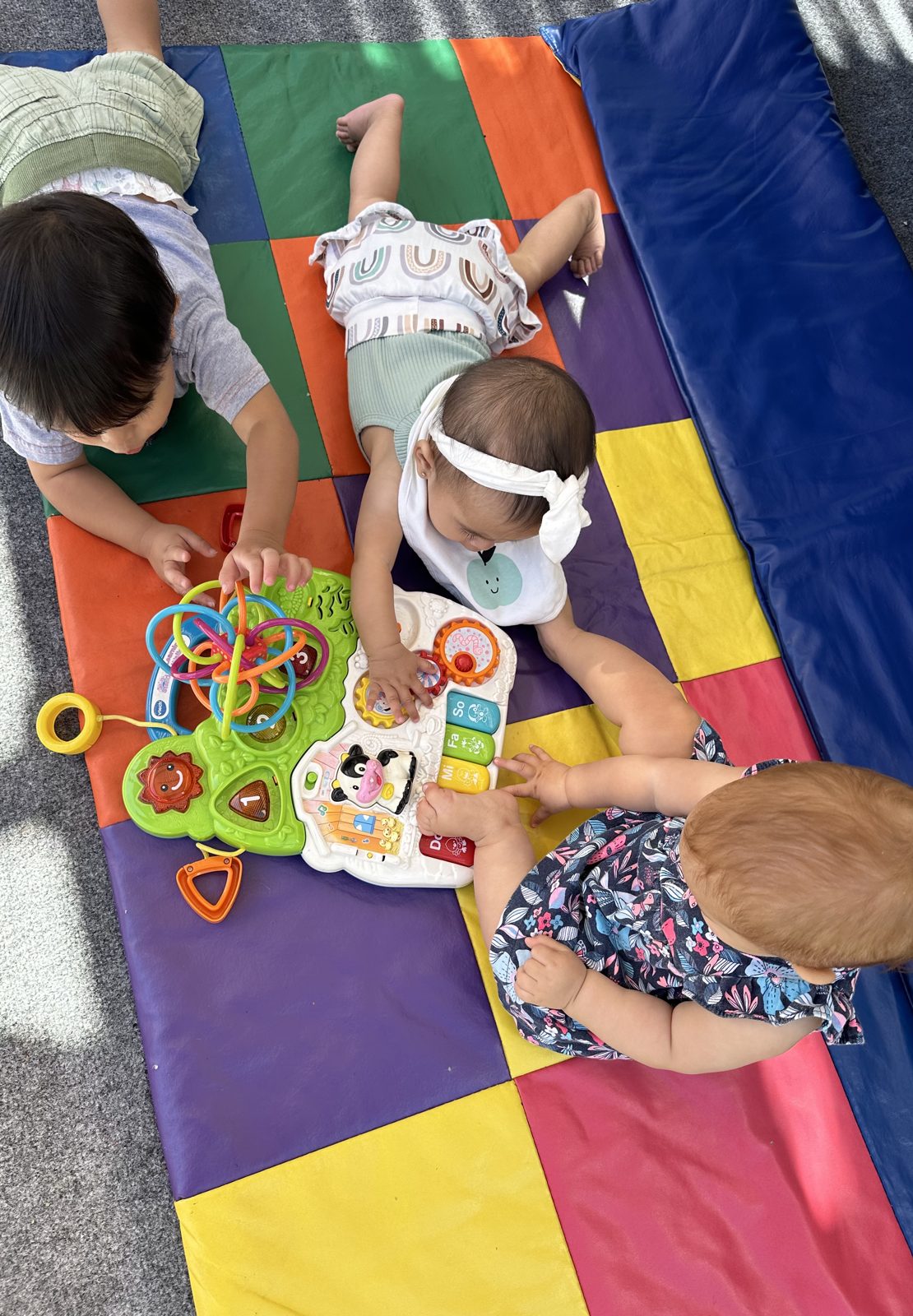 Babies exploring activity toys together on a colorful play mat