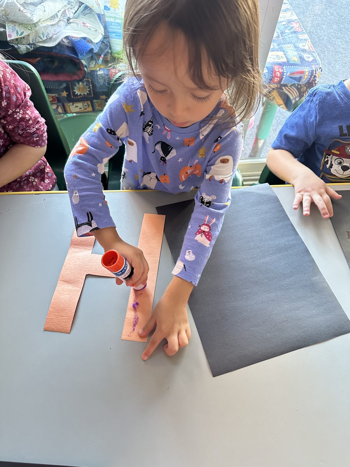 Preschooler gluing a letter H onto construction paper during letter practice