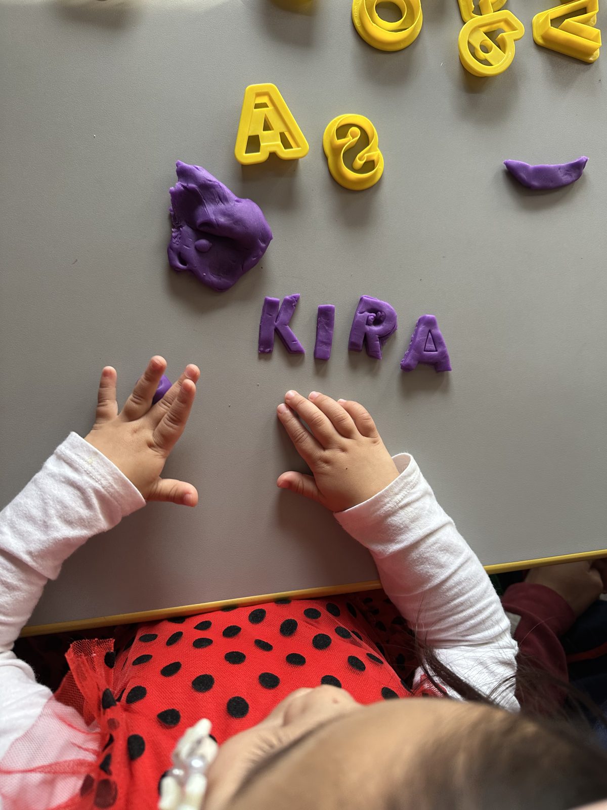 Toddler spelling her name with purple play dough letters