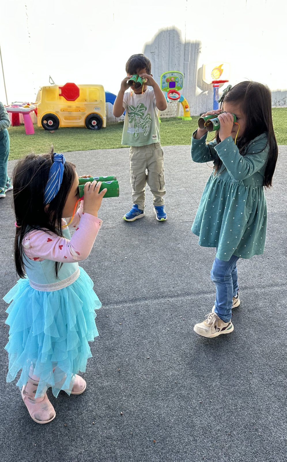 Three preschoolers exploring outside with handmade paper binoculars