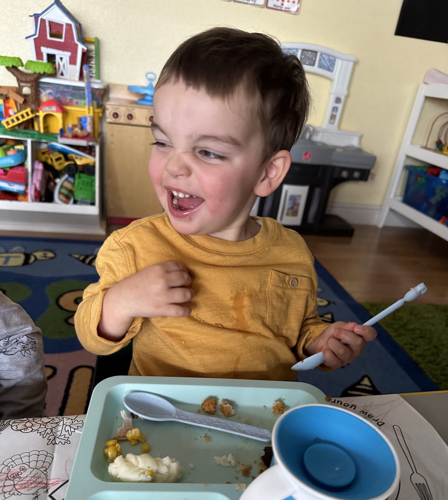 Happy toddler laughing during a home-cooked lunch at the daycare table
