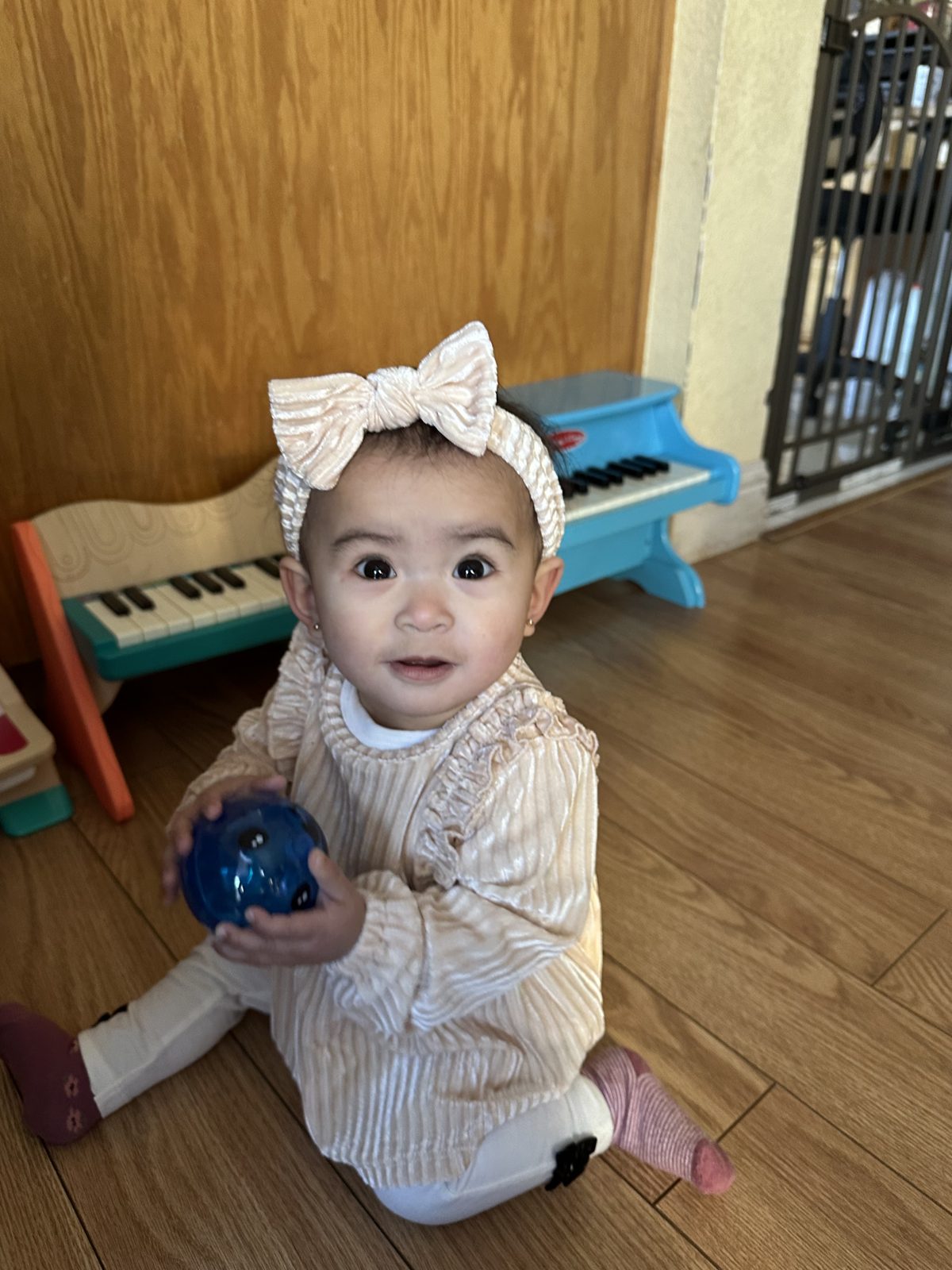 Smiling baby sitting by the toy piano holding a ball
