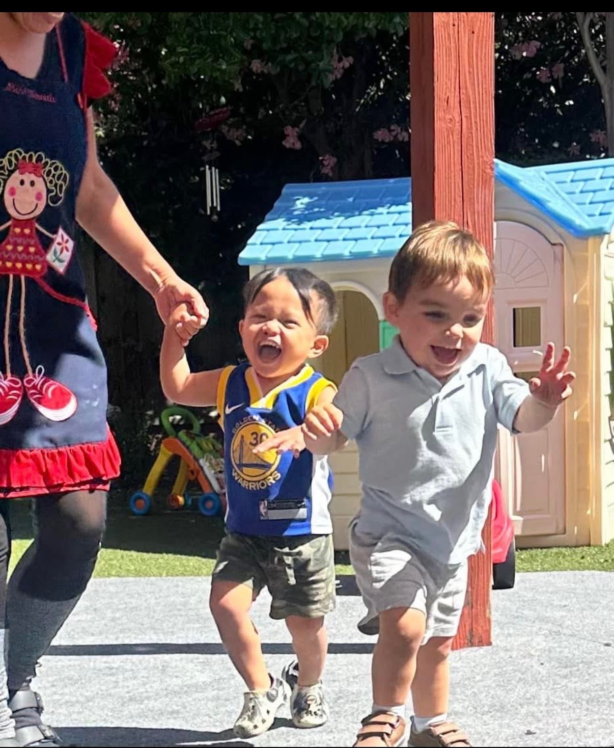 Two toddlers laughing as they walk hand in hand outside at Crayoland Daycare